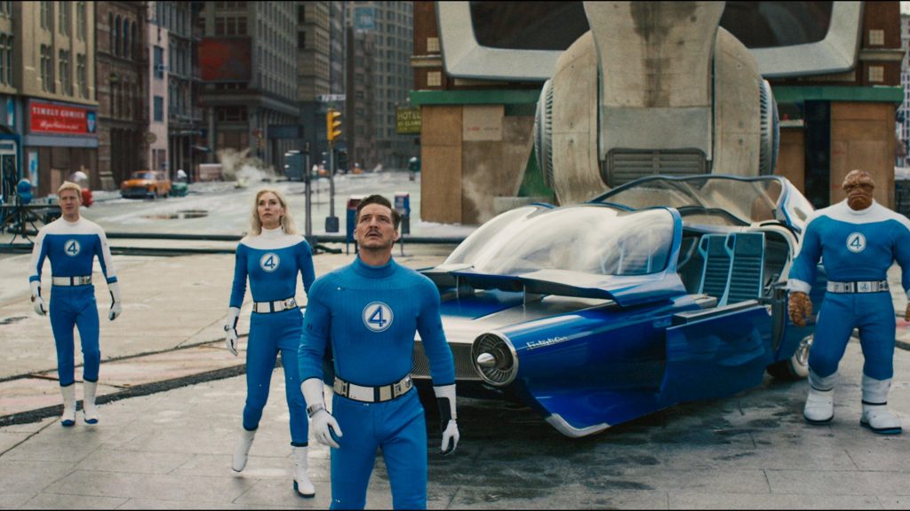 A still image from The Fantastic Four: First Steps showing the four main characters in their fantastic four uniforms standing the street staring up at something.